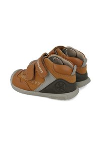 Zapatos de cuero marrón para niños pequeños con correa de Velcro, acentos grises y un interior acolchado. Presentan una suela de goma texturizada y un diseño cosido.