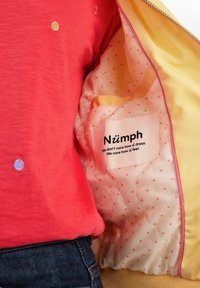 Röd topp med färgglada prickar, i kombination med en gul kant med rosa prickar. Etiketten säger "Nümph" med en svart textslogan inuti.