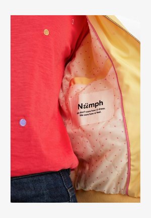 Rotes Oberteil mit bunten Punkten, kombiniert mit einer gelben Einfassung mit pinken Polka-Dots. Das Etikett trägt die Aufschrift "Nümph" mit einem schwarzen Textslogan im Inneren.