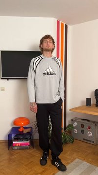 Gray long-sleeve mesh Adidas shirt with black logo and stripes, paired with black sweatpants and black Adidas sneakers, standing indoors.