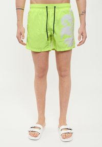 Costume da bagno verde lime realizzato in tessuto leggero, con un design astratto bianco, vita elasticizzata con cordino nero e tasche laterali.