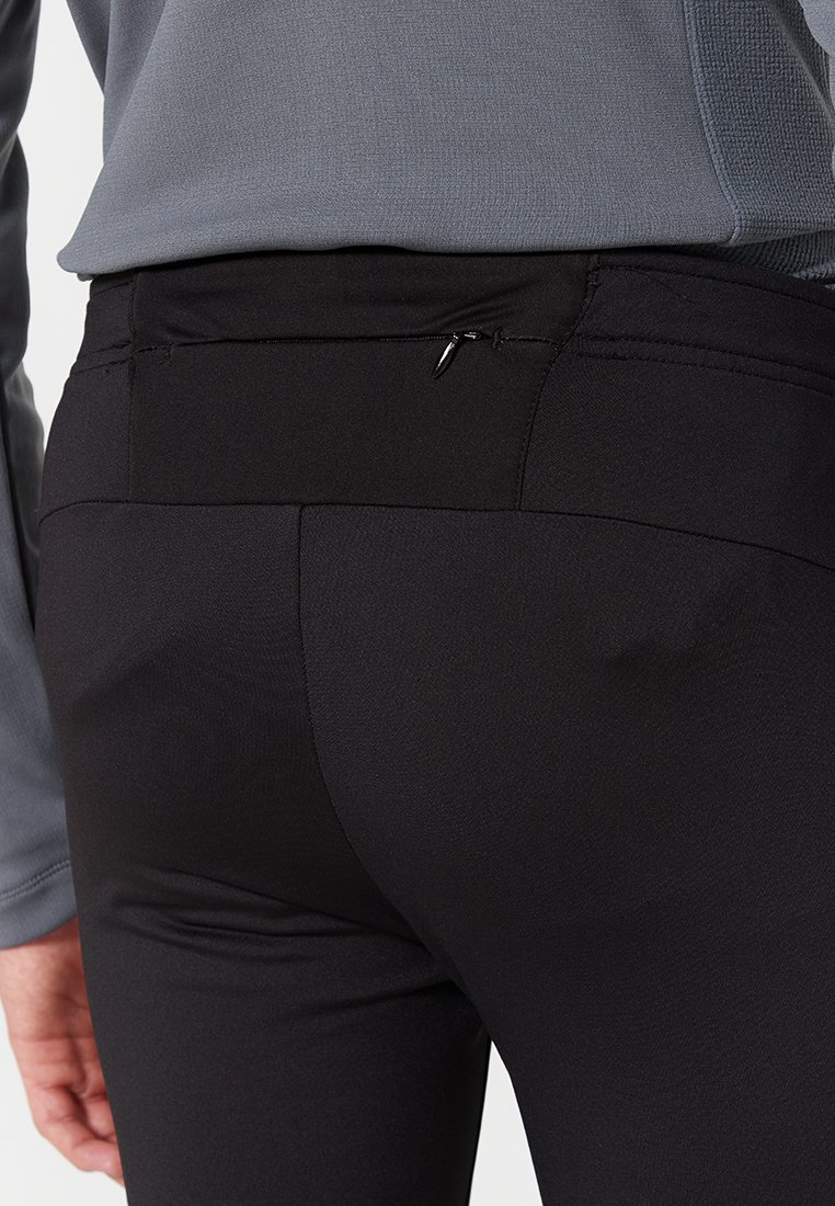 Pantaloni sportivi neri con una texture liscia, dotati di una tasca con zip discreta sulla vita posteriore. Il tessuto sembra elastico e aderente.