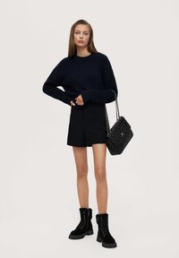 Navy ribbed sweater, black tailored shorts, black quilted handbag with chain strap, and black lace-up boots with fur trim.
