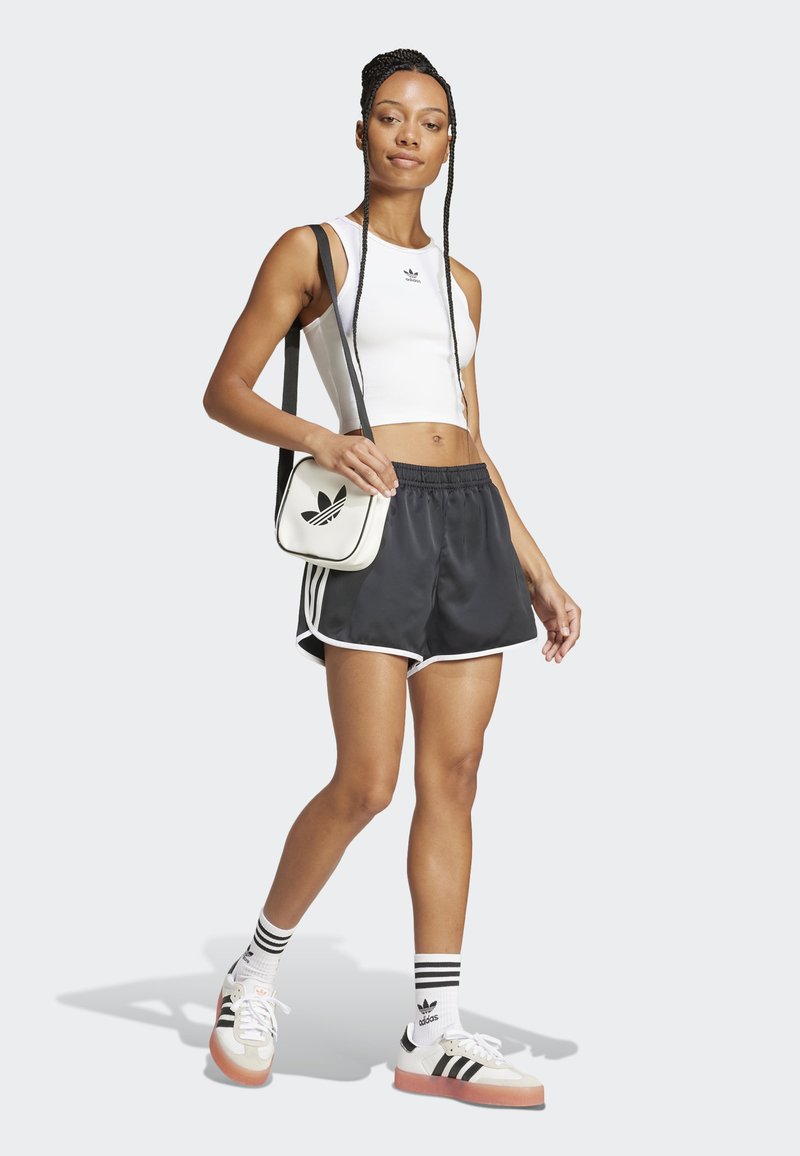 Svarta idrottsshorts med vit kant, tillsammans med en vit crop top. En svart och vit axelväska och randiga strumpor fulländar looken.