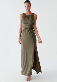 Vestido maxi verde oliva con corpiño ajustado, escote plisado, cintura con cinturón y abertura lateral. Tela texturizada; diseño sin mangas.
