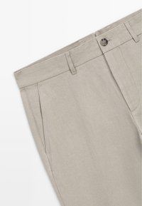 Pantalon beige avec passants pour ceinture, poches latérales avant et fermeture à bouton visible à la taille.