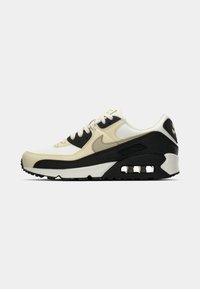Air Max 90 tossud, millel on valge ja kreemikas ülemine osa, mustad tekstureeritud detailid ning nähtav õhkkattega moodul vahetallal.