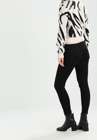 Černé úzké džíny s vysokým pasem, doplněné o krátký svetr s černobílým vzorem a černé kotníkové boty. Hladká textilie.