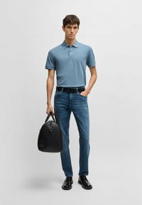 Ljusblå pikétröja, mörkblå jeans, svarta läderskor och en svart väska. Pikétröjan har krage och korta ärmar, med en logotypdetalj.