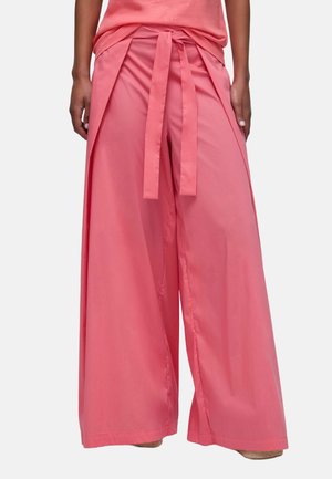 Kobieta nosząca różowe szerokie spodnie z wiązanym paskiem w talii, w zestawieniu z dopasowanym różowym topem.