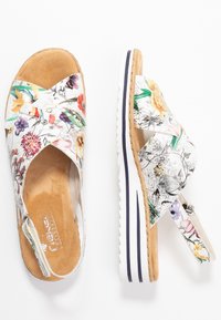 Blommönstrade sandaler med korsremmar, tillverkade av mjuka material. De har en vadderad fotbädd och en vit plattformssula med marinblå accenter.