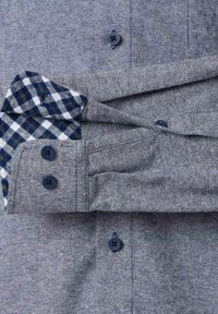 Męska koszula zapinana na guziki w szarej tkaninie w jodełkę, z niebieską i białą kratką wewnątrz mankietów, z granatowymi guzikami i mankietami.