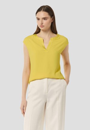 Yellow short-sleeve blouse with a V-neckline, smooth fabric, loose fit, and minimalist design, paired with cream-colored trousers.