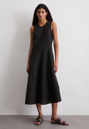 Black linen sleeveless dress with a round neckline, A-line silhouette, and mid-calf length. Paired with dark sandals featuring a gold accent.