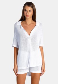 Vit stickad skjorta med krage, korta ärmar och avslappnad passform, i kombination med matchande shorts. Lätt och texturerad tyg.