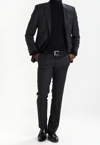 Completo nero e dolcevita, pantaloni slim fit, scarpe nere lucide, texture sottile nel tessuto, dettagli minimi, design classico su misura.