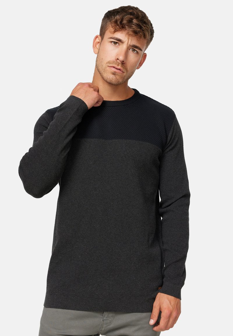 Mørk grå sweater med en tekstureret krop og en glat, ensfarvet topanel. Lange ærmer og en rund halsudskæring med en subtil brandingdetalje.