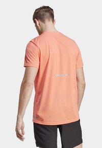 Camiseta atlética de manga corta en un brillante color coral, confeccionada con tela que absorbe la humedad, con una franja reflectante en la parte posterior y un corte estándar.