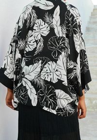 Czarna i biała bluzka w stylu kimono z dużymi, tropikalnymi wzorami liści, luźny krój, zwiewne rękawy i gładka tekstura materiału.