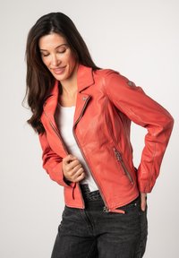 Rode leren motorjack met ritssluitingen en een reverskraag, gecombineerd met een wit shirt en donkere jeans. Soepele textuur, slanke pasvorm.