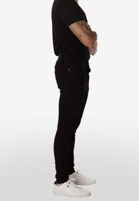 Vaqueros negros de corte ajustado hechos de denim, con cinco bolsillos y cierre de cremallera. Combinados con zapatillas blancas para contrastar.