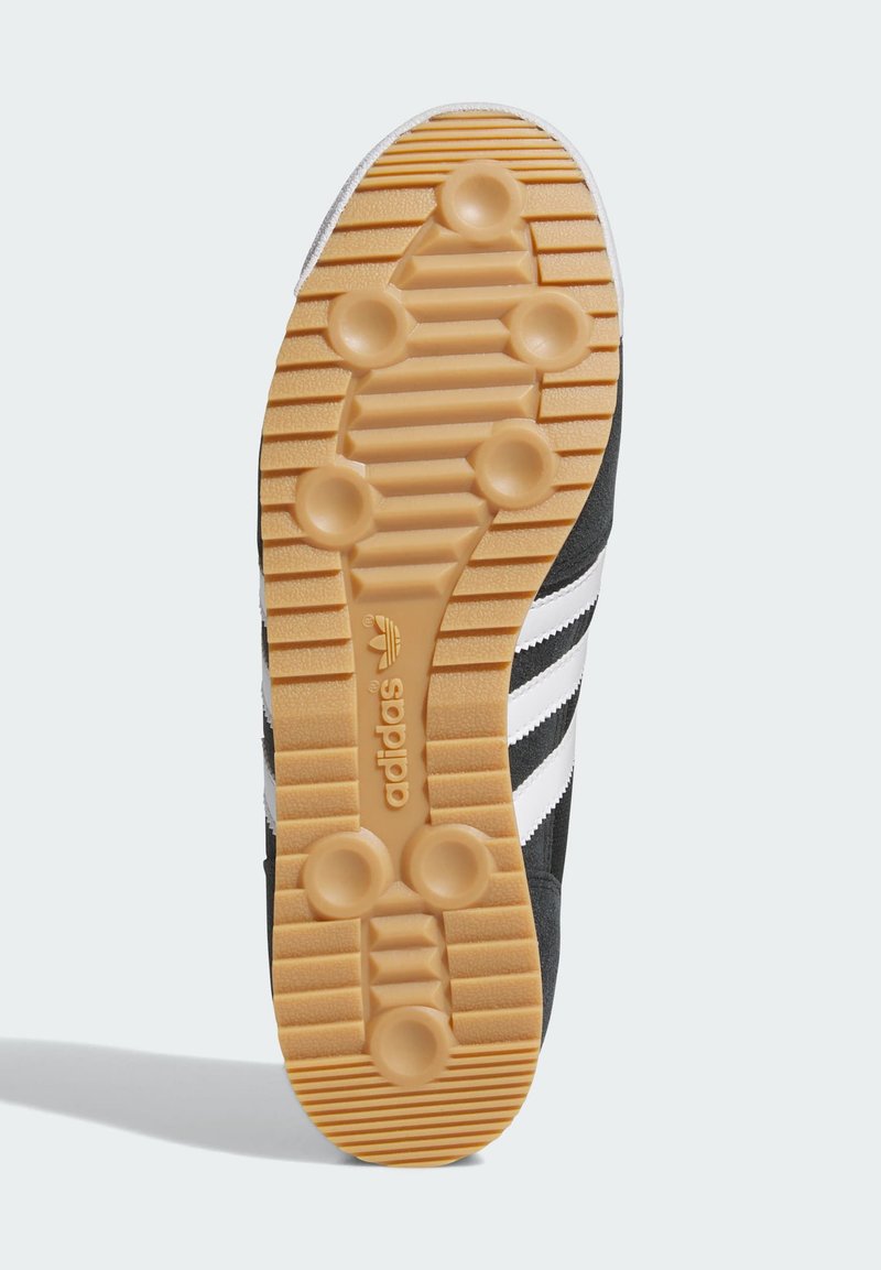 Schuhsohle aus Gummilaufsohle mit kreisförmigen Noppen und Rillen, Adidas-Logo in der Mitte geprägt, schwarzes Obermaterial mit sichtbaren weißen Streifen.