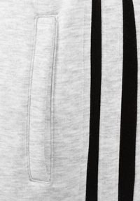 Lichtgrijze sweatpants met een gestructureerde stof, een zijzak en twee zwarte verticale strepen langs de buitennaad.