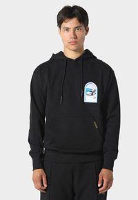 Sudadera de algodón negra con un bolsillo frontal, cordones ajustables y un gráfico colorido en el pecho que presenta un vehículo y un paisaje.