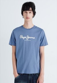 Šviesiai mėlynas medvilninis marškinėlis su balta išsiuvinėta "Pepe Jeans London" logo. Trumpomis rankovėmis ir apvaliu kaklu, su laisvu siluetu.