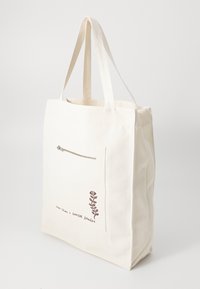 Canvas tote bag in off-white with a brown zip pocket and floral design. Features sturdy handles and a spacious interior for carrying items.