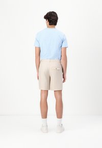 Light blue short-sleeve shirt paired with beige striped shorts featuring a back pocket. Model wears white socks and light sneakers.