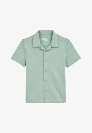 Rövid ujjú, világoszöld gombos ing, puha anyagból készült. Kerek nyakkal és hat gombbal rendelkezik az elején. Egyszerű, texturált mintázat.