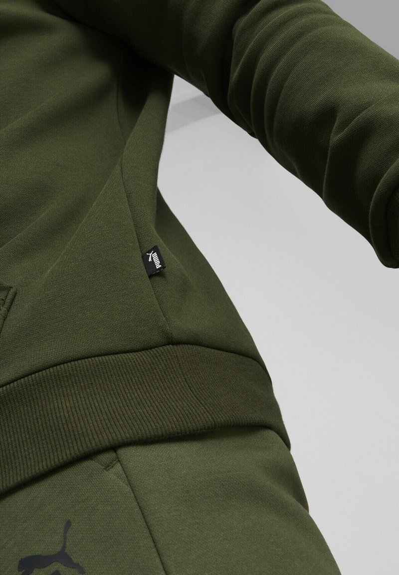 Olivgrön sweatshirt med ribbad mudd, sidoficka och liten svart logotag. Mjuk, texturerad tyg med synliga sömdetaljer.