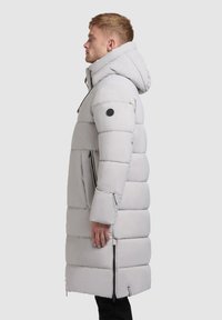 Hellgrauer langer Puffermantel mit Kapuze, horizontal gestepptem Design, Reißverschlusstaschen an den Seiten und einem runden Logoakzent am Ärmel.