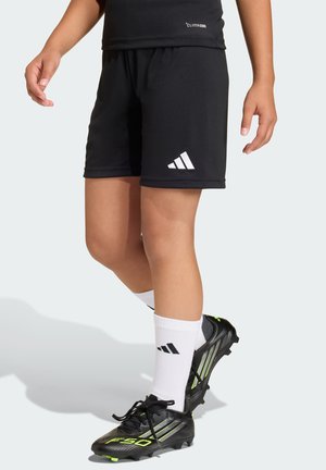 Schwarze Sportshorts mit weißem Adidas-Logo, kombiniert mit schwarzen Stollenschuhen mit grünen Akzenten und weißen Socken mit dem Adidas-Logo.
