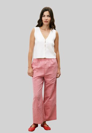Haut sans manches blanc avec un décolleté en V et des boutons à l'avant, associé à un pantalon large à rayures roses. Des chaussures plates rouges complètent la tenue.