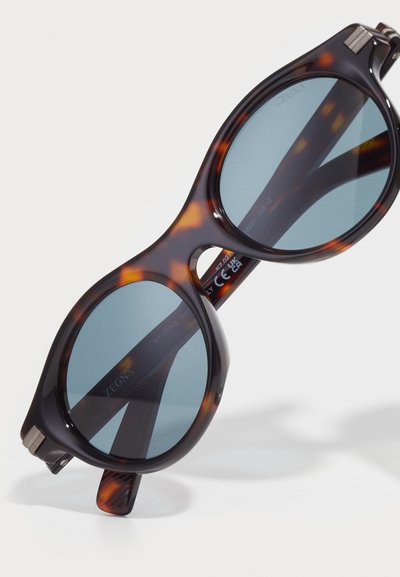 Tortoiseshell sunglasses with oversized rounded lenses. Blue tinted lenses with a thick frame featuring metal accents at the temples.
