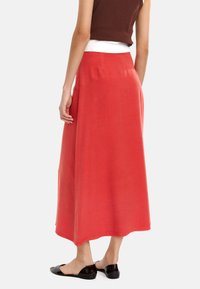 Czerwona midi spódnica o gładkiej fakturze, z wysokim stanem i bocznymi kieszeniami. Połączona z czarnymi butami wsuwanymi.