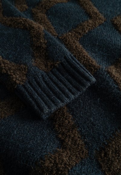Sweter dziany z ciemnoniebieskim tłem i brązowymi geometrycznymi wzorami, z teksturowanym prążkowanym mankietem dla dodatkowego detalu i ciepła.