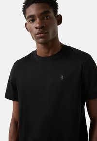 Czarny krótki rękaw t-shirt wykonany z miękkiej tkaniny, z subtelnym wytłoczonym logo na lewej stronie klatki piersiowej, z klasycznym okrągłym dekoltem.