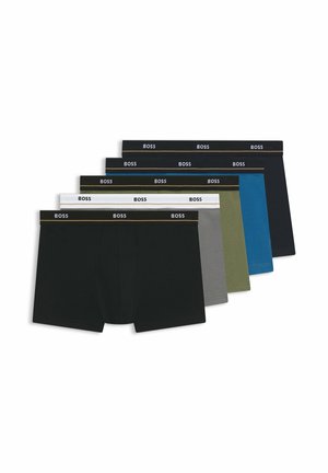 Junger Mann mit kurzen Haaren, trägt schwarze BOSS Boxershorts, steht vor einem schlichten weißen Hintergrund.