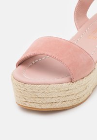 Rosa mockaskinn öppen tå sandal med ett brett band, som har en vävd juteplattform och gummisula. Sömdetaljer längs kanterna.