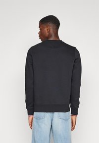 Felpa nera a girocollo in cotone, con polsini e orlo a coste, indossata con jeans azzurri, mostrata di spalle.