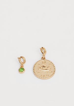 Gold-tone earrings featuring a large, textured circular pendant with a design and a smaller charm set with a green stone.