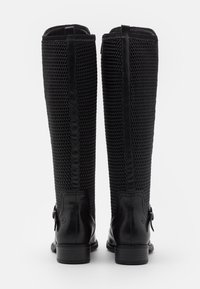 Botas negras hasta la rodilla con un upper de malla de acabado texturizado, acentos de cuero y un pequeño lazo decorativo en la parte posterior.