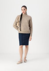 Beige stickad tröja, hög krage, ribbad fåll; mörk denim blyertskjol, beige lägenheter med ankelremmar; inomhus, neutral bakgrund.