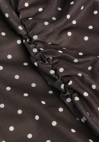 Tela marrón oscuro con lunares blancos, fruncida y cosida para crear pliegues texturizados y un efecto arrugado.