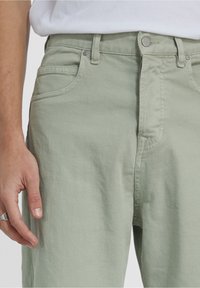 Pantalones de algodón verde claro con un cierre delantero de botón, diseño de cinco bolsillos y una tela lisa con una ligera textura.