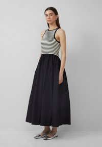 Maxikleid mit gestreiftem Oberteil und einfarbig schwarzem Rock. Mit Rundhalsausschnitt, tiefem Taillenbund und Seitentaschen. Trägt dazu silberne Schuhe.