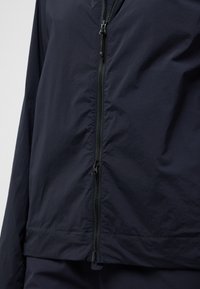 Giacca zip-up di colore blu navy con una texture leggera e liscia. Caratterizzata da una cerniera nera centrale e un orlo dritto. Design minimale senza motivi.